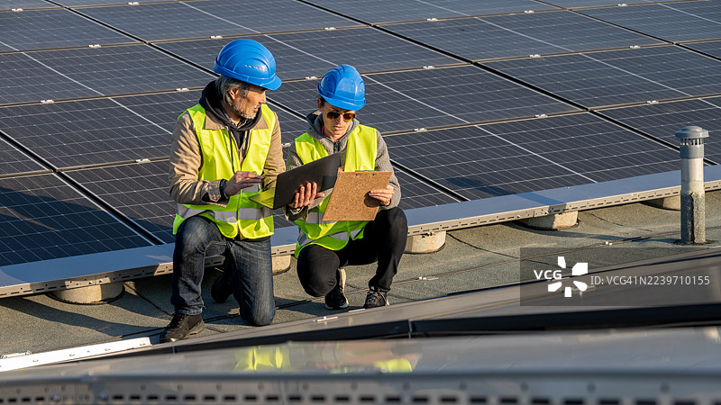 亚洲男性和高加索女性专家评估屋顶太阳能装置图片素材