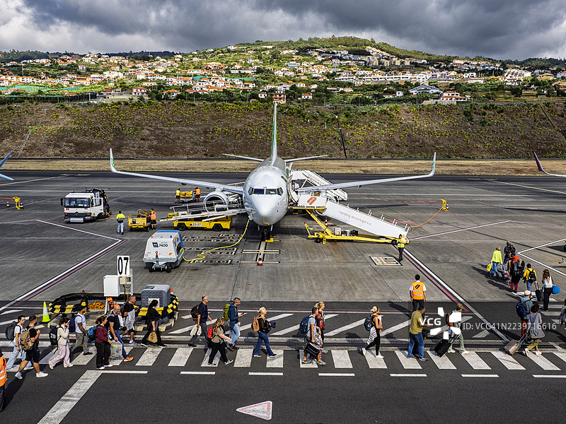 乘客们正在马德拉岛的丰沙尔机场跑道上登上停靠的飞机。图片素材