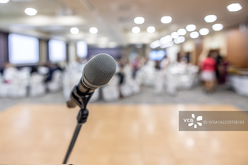 前景中的麦克风架清晰对焦，背景虚化处为会议室，有桌椅和舞台，暗示已为活动或演示做好准备。图片素材