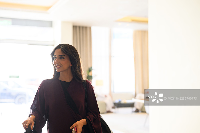 快乐的年轻女旅行者穿着传统服装，在明亮的酒店室内行走时面带微笑图片素材