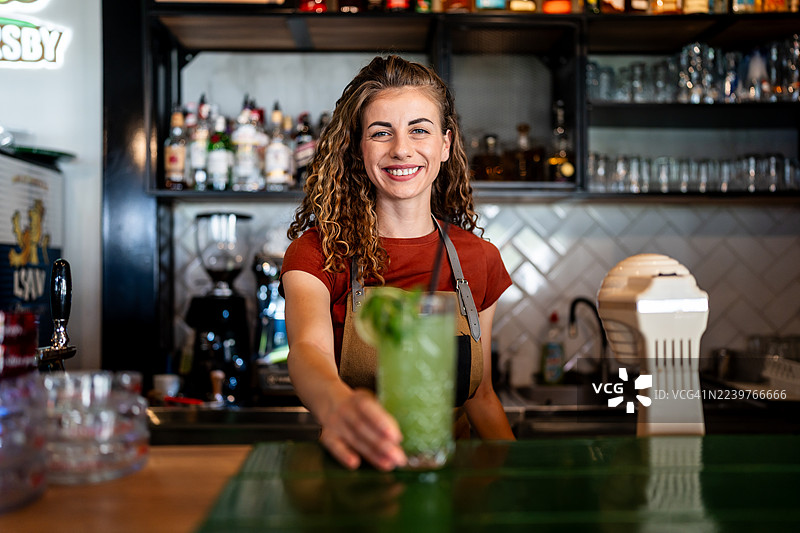 调酒师微笑着在吧台后面调制鸡尾酒图片素材