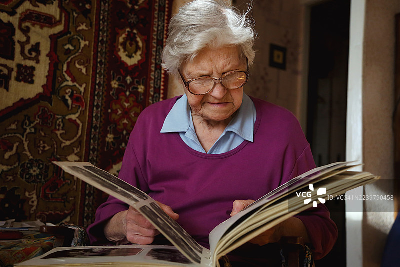 一位白发长者在家翻看复古相册，深情回忆往昔图片素材