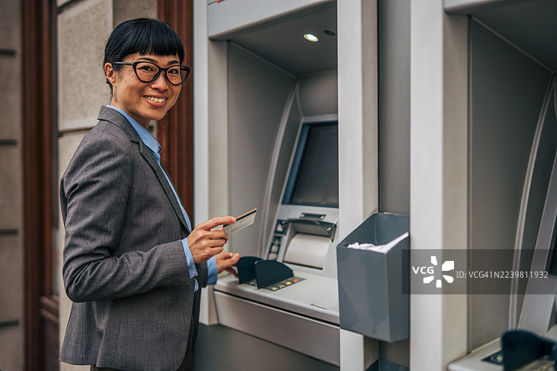 一名女子在使用ATM机时，一边刷卡一边微笑。图片素材