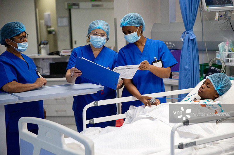 医生和护士在医院重症监护室查看一名少女的病历图片素材