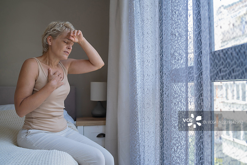 一个女人坐在床上，手放在额头上，陷入沉思。图片素材