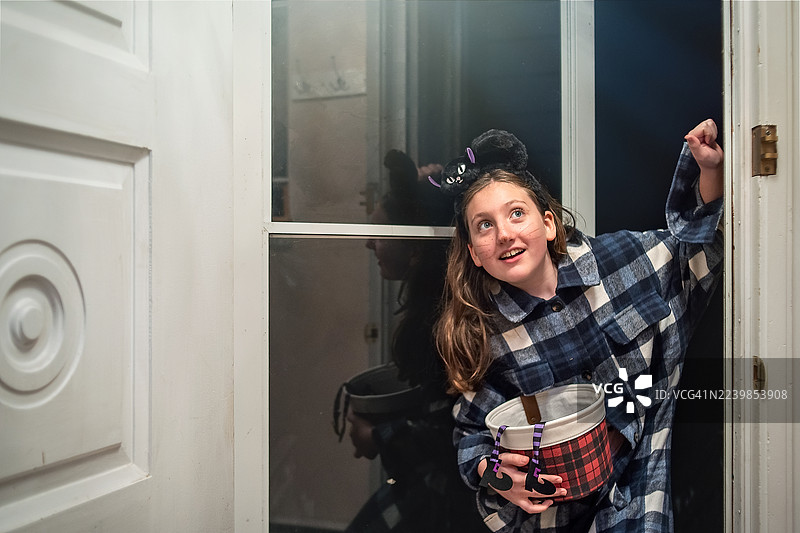 宾夕法尼亚州波科诺斯地区，一个兴奋的十来岁的孩子提着糖果篮在门口讨要万圣节糖果。图片素材