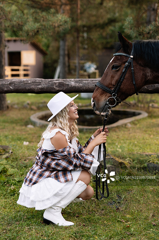 穿着牛仔帽的金发美女在乡村的牧场或马厩与马站在一起图片素材