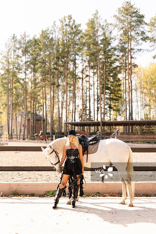 身穿牛仔帽的美丽金发女郎，在乡村的牧场或马厩里与马站在一起。图片素材