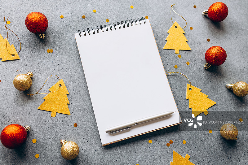 圣诞节平面图，包含空白螺旋笔记本、圣诞装饰和一支笔，背景为灰色。非常适合节日主题设计、贺卡或书写圣诞愿望清单。图片素材