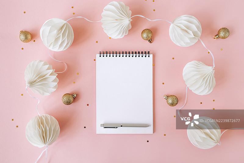 粉色背景上的圣诞节平面图，包含空白螺旋笔记本、圣诞装饰品和一支笔。非常适合节日主题设计、贺卡或书写圣诞愿望清单。图片素材