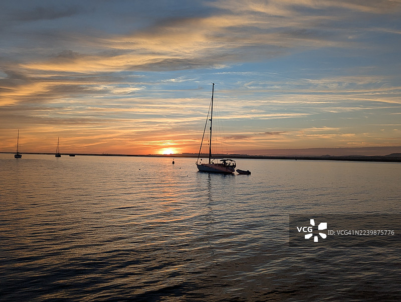 夕阳下，帆船在葡萄牙阿尔加维的库拉特拉岛前抛锚图片素材