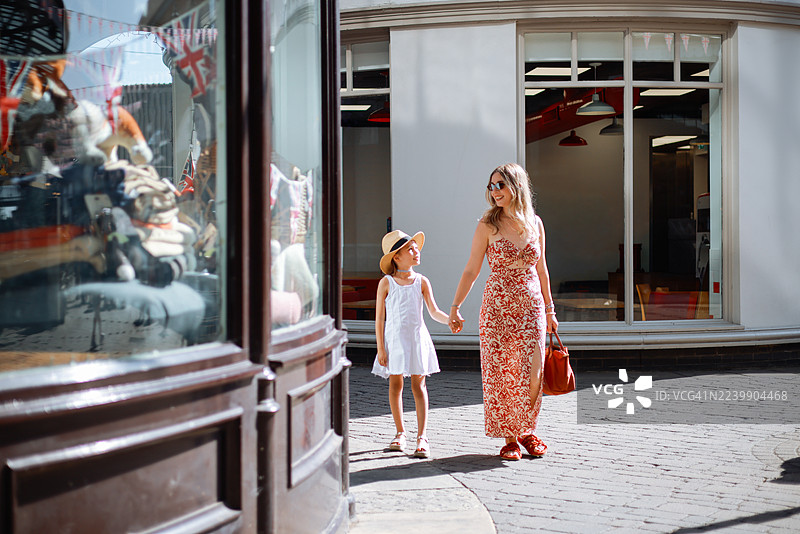 年轻的母亲和她可爱的女儿一起走在伦敦街头，背景是红色的城市巴士。图片素材