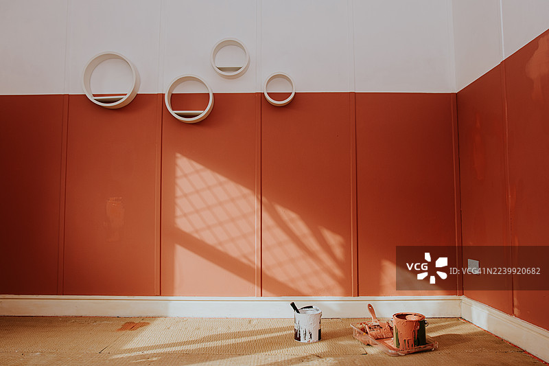 房间的广角镜头，刚粉刷过，墙面选择了赤陶土色。画笔和颜料罐散落在墙前的地板上。图片素材