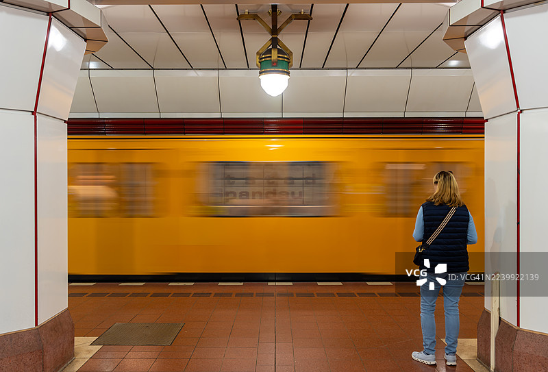 一名女子站在站台上，望着一辆即将到来的地铁列车，画面为后视图。图片素材