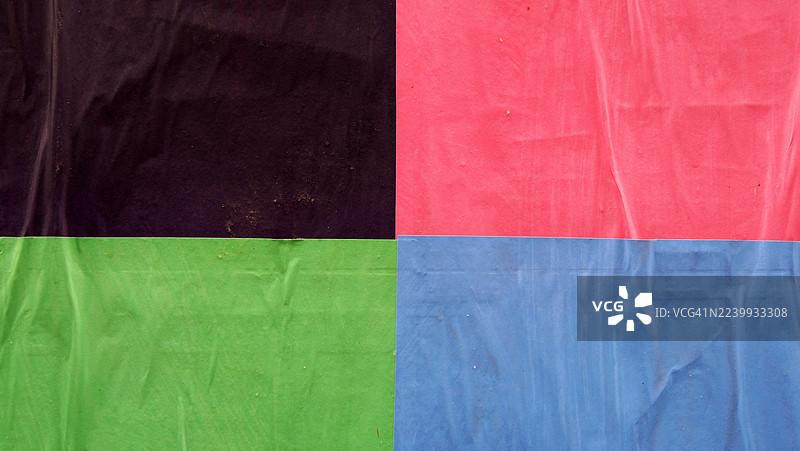 特写镜头,墙上贴有黑色、红色、绿色和蓝色海报,海报呈波浪状。粗糙的纹理。阳光。自然色彩。比利时布鲁塞尔。全画幅 16:9图片素材