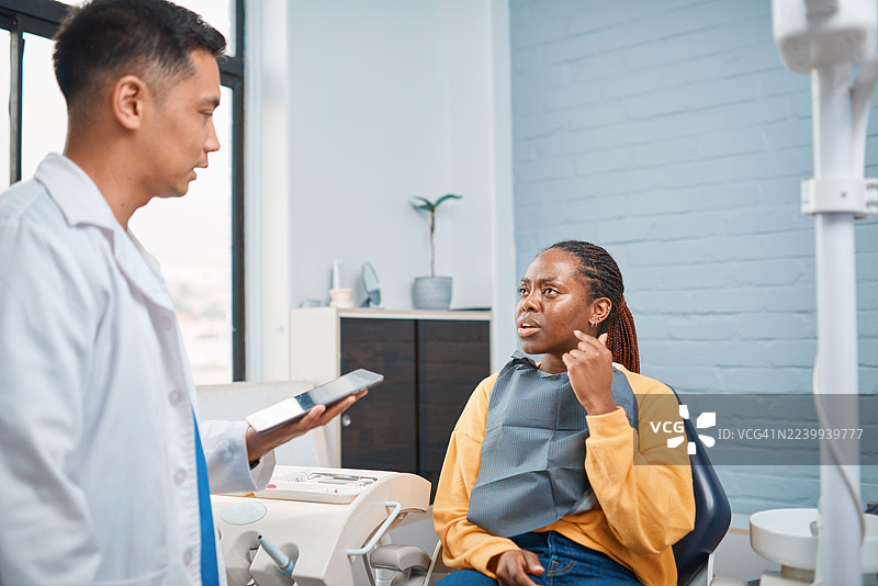 一位亚洲牙医在现代诊所与年轻的黑人患者讨论治疗方案图片素材