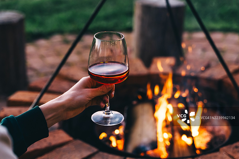 手中握着一杯酒，旁边是炉火。度假的夜晚。图片素材