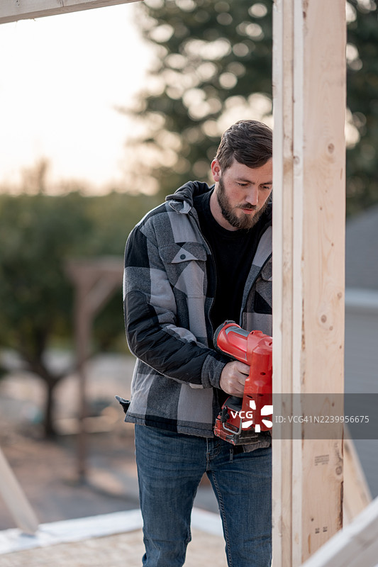 白种人建筑工人户外使用红色电动钉枪在木框上作业，专注且安全图片素材