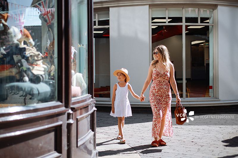 年轻的母亲和她可爱的女儿一起走在伦敦街头，背景是红色的城市巴士。图片素材