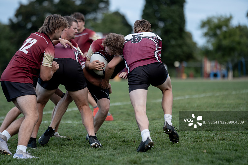 绿色球场上，橄榄球运动员在团队比赛中进行擒抱和推挤——多元化运动员拼尽全力。Rugby Players Tackle and Push During Team Match on Green Field – Diverse Players Playing Hard图片素材