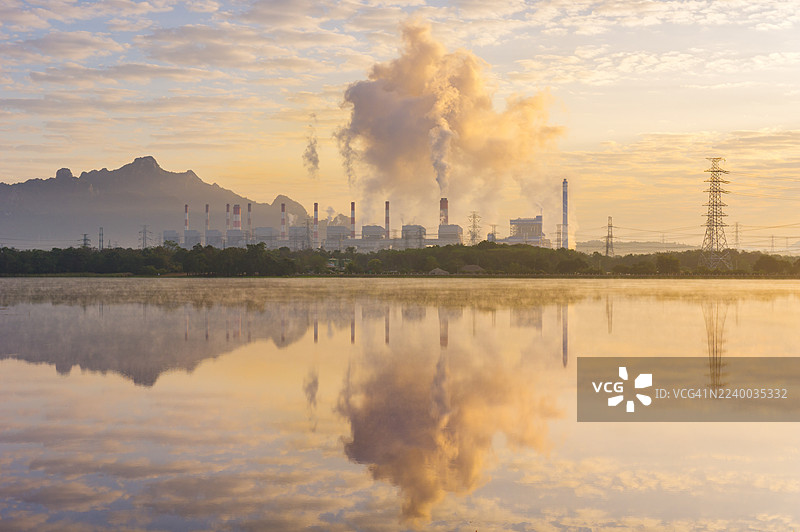 泰国兰邦府，暮色下的湄莫发电厂。燃煤电站的蒸汽烟雾与薄雾倒映在湖水中，突显了泰国北部的工业、能源和环境影响。图片素材