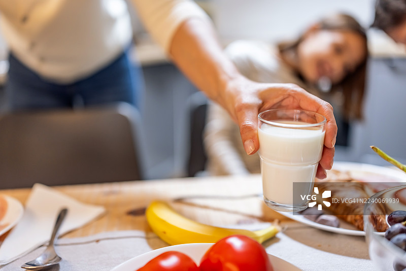 一家人在早餐桌上分享牛奶，桌上还有新鲜水果和糕点图片素材