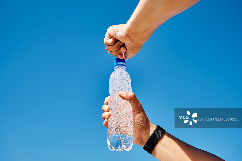 男人的双手在蓝天下打开一瓶塑料瓶装的苏打水。图片素材