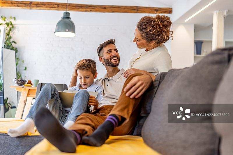 快乐的一家人在沙发上放松，孩子在玩平板电脑，父母充满爱意图片素材