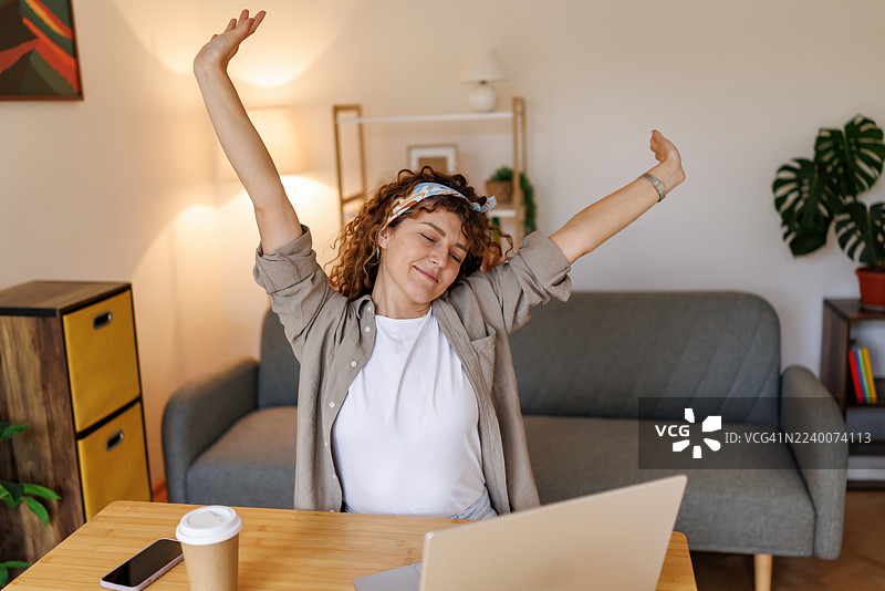 家庭办公室里，一位中年女性在高效工作一天后伸展身体的肖像图片素材