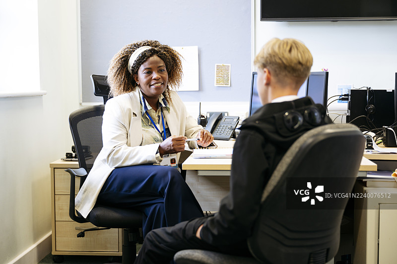 中学校长在办公室里对一名十几岁的男孩微笑，鼓励、支持、关怀图片素材