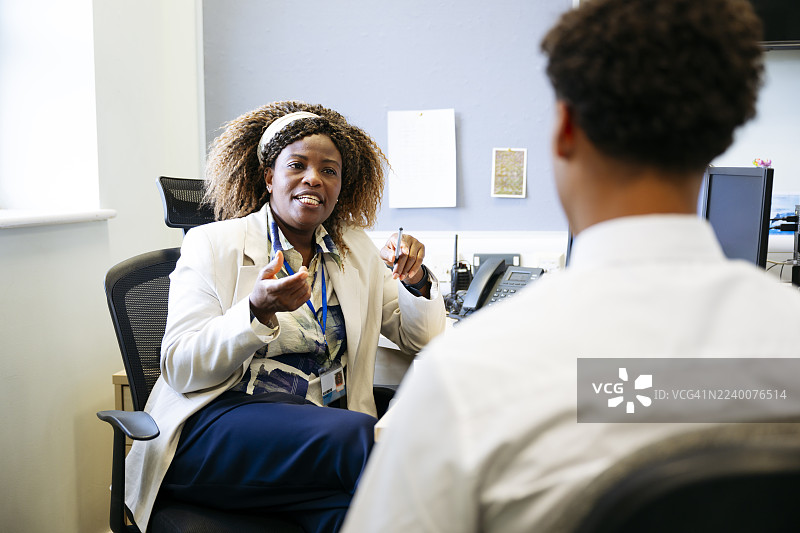 学校老师在办公室向一名男学生解释并打手势图片素材