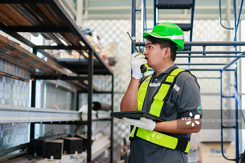 工程师或仓库工作人员穿着安全装备，在工厂的货架上使用数字平板电脑检查库存，代表物流管理、仓库运营和库存控制。图片素材