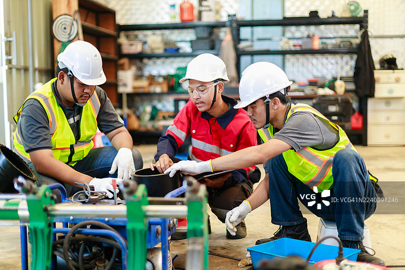 三名身穿安全防护装备的工程师，在工业车间使用液压对接焊机讨论 HDPE 管道连接，重点关注团队合作、规划和管道安装流程。图片素材