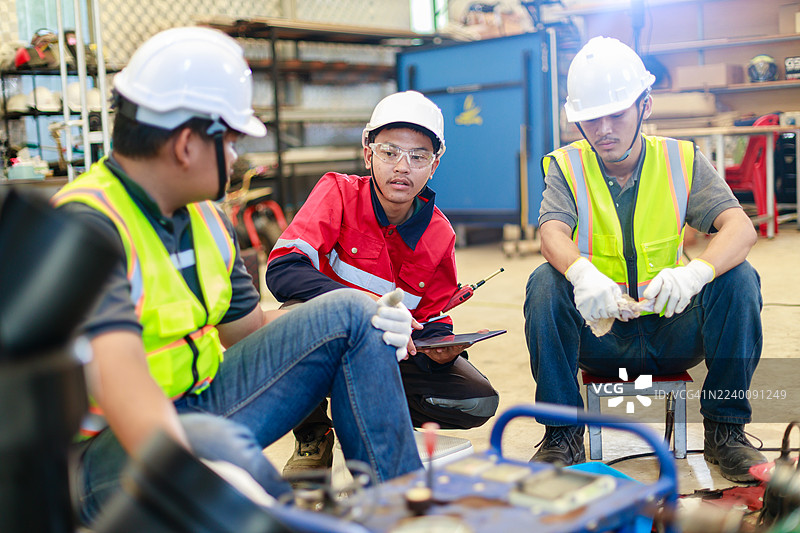 三名身着安全装备的工程师在工业车间使用液压对接焊机讨论HDPE管道连接，重点关注团队合作、规划和管道安装过程。图片素材