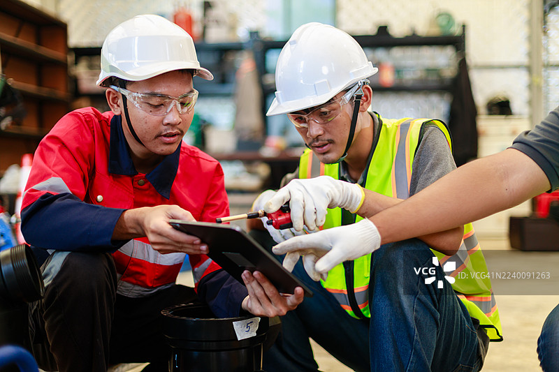三名身着安全防护装备的工程师在工业车间使用液压对接焊机讨论HDPE管道连接，重点关注团队合作、规划和管道安装流程。图片素材