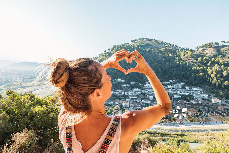 女子在风景如画的小镇景观上做出心形手势图片素材