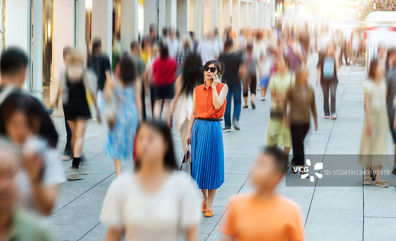 时髦女子在繁忙的街道上使用智能手机行走图片素材