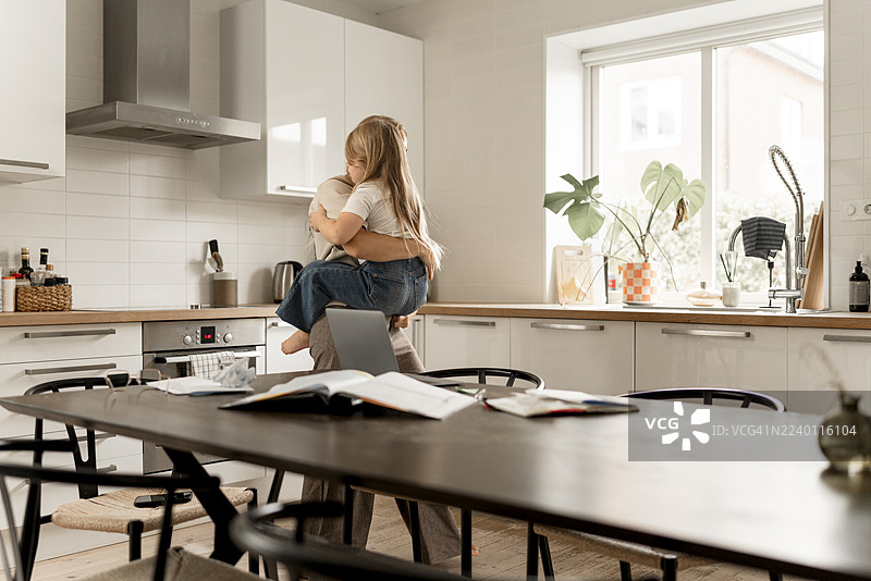 家庭生活：一位斯堪的纳维亚母亲在温馨的厨房里与孩子相处，平衡工作与生活（或育儿）。图片素材