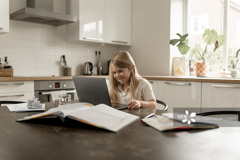 年轻女孩在家用笔记本电脑学习，而母亲则在工作和家庭事务之间取得平衡。图片素材