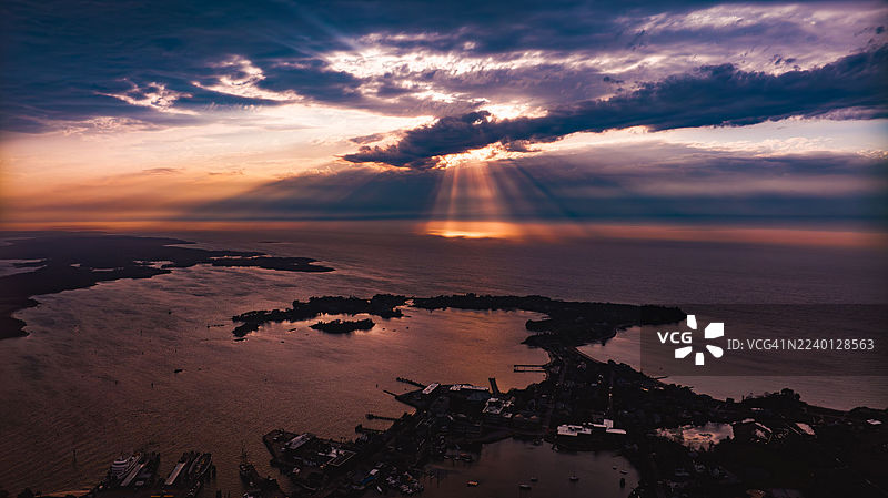 马萨诸塞州东法尔茅斯附近伍兹霍尔的北大西洋上空，壮丽的日落神光照耀着海岸和树林。图片素材