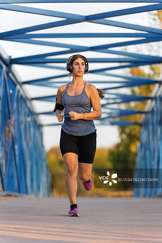 戴着耳机在蓝色桥上跑步的女性图片素材