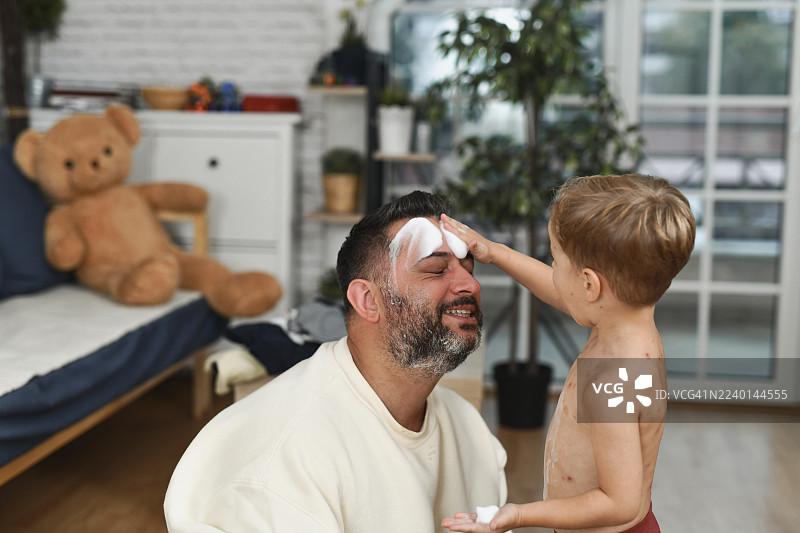 父亲和儿子在家中一起开怀大笑，孩子摸着爸爸的脸。图片素材