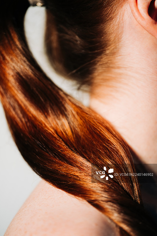 特写镜头，展示了某人闪亮的红色马尾辫，柔和的阳光突显了其丰富的色彩和质感。图片素材