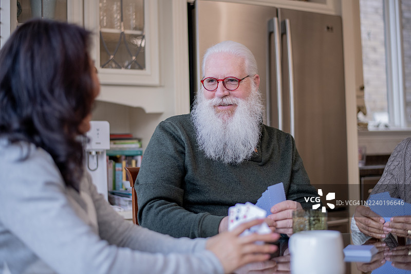 年长朋友们在温馨的厨房里玩纸牌游戏，分享欢笑与交谈图片素材