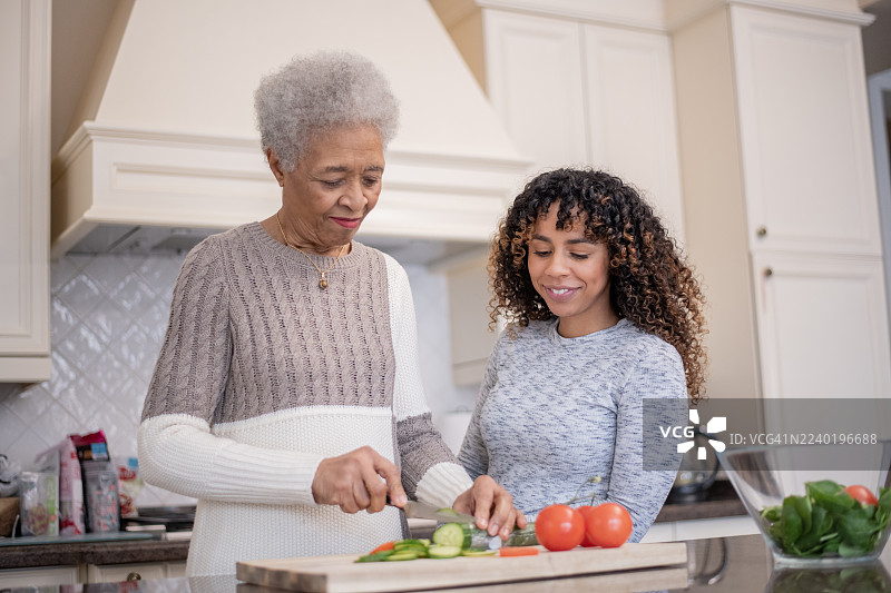 祖母和孙女在现代厨房里一起烹饪，旁边有新鲜的西红柿图片素材