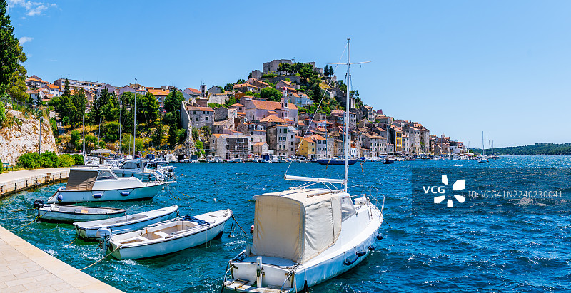 碧空下，希贝尼克码头全景，船只停泊在水边和古老的联排房屋附近图片素材