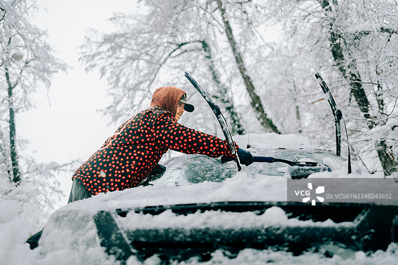 暴风雪中，一名男子正在清理汽车挡风玻璃上的积雪。图片素材