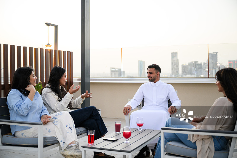 一群年轻人在屋顶上享用饮品，在轻松的夜晚背景下，欣赏着城市天际线的美景。图片素材