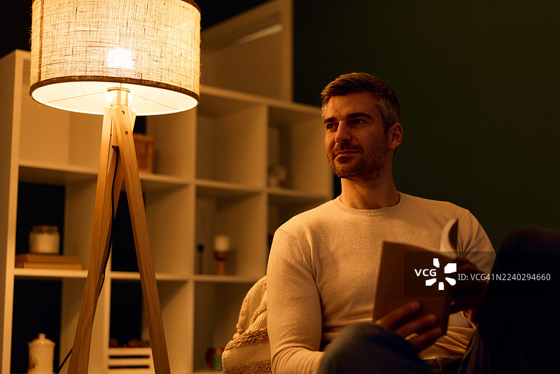 男人在家放松地在灯旁读书图片素材