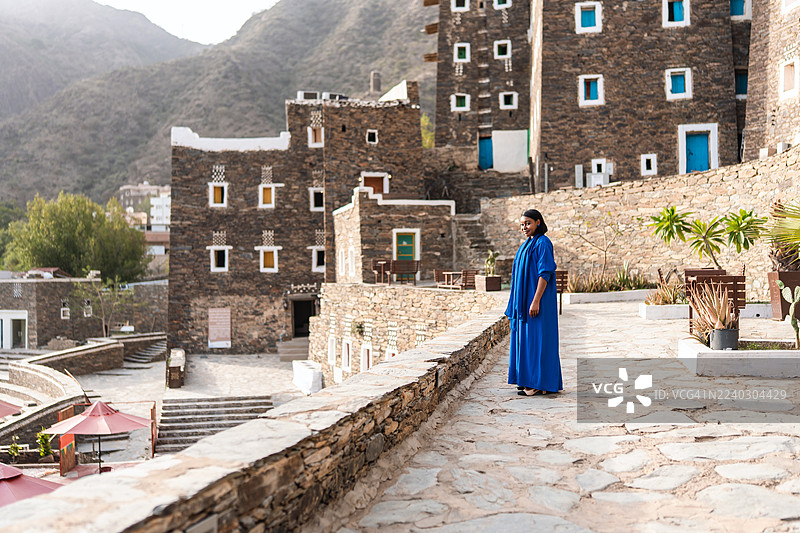 中年黑人女性身穿鲜艳的蓝色阿巴亚，探索里贾尔阿尔马（Rijal Almaa）的建筑图片素材